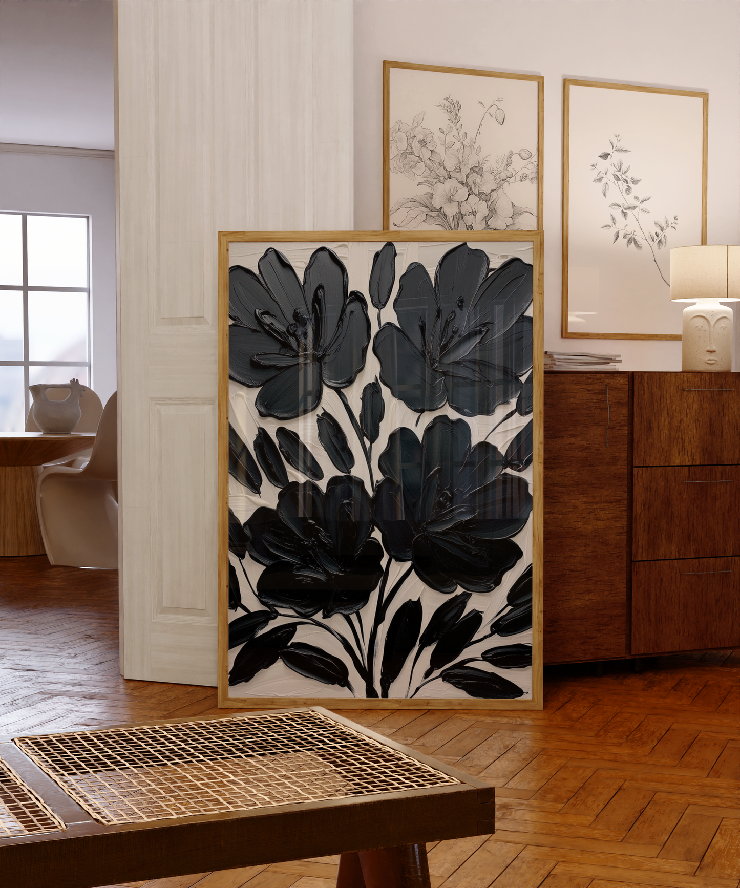 Black floral wall art abstract flower print leaning against a console table in a modern interior with wood flooring and framed art