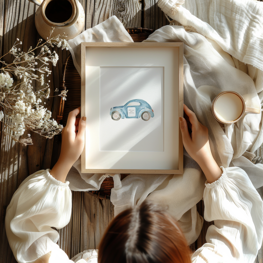 Blue car nursery wall art print with the words ‘Little racer big dreams,’ displayed in a wooden frame and held in hands on a flatlay scene with fabric, flowers, and coffee. Boys’ nursery or playroom decor, available as framed or canvas print.