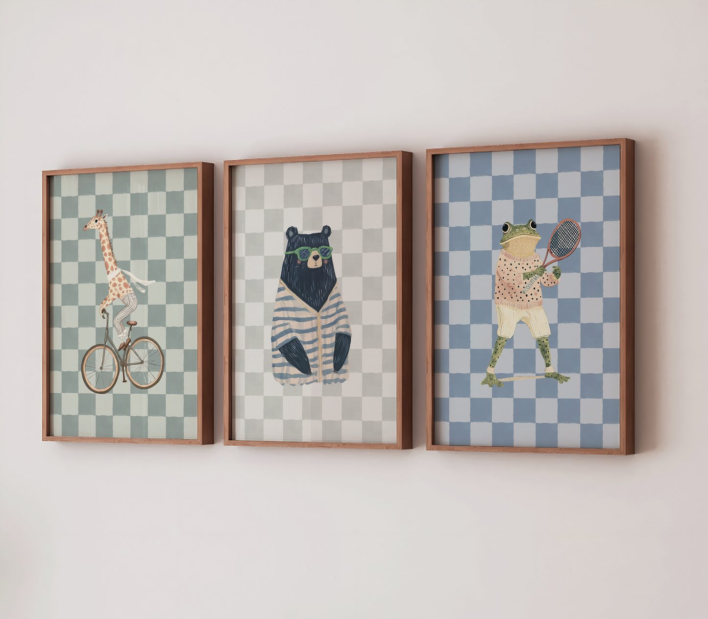 Set of three framed nursery wall art prints – giraffe on a bike, bear in sunglasses, and preppy frog playing tennis – displayed on a wall with wooden frames. Funky boys’ nursery, bedroom, or playroom wall decor.