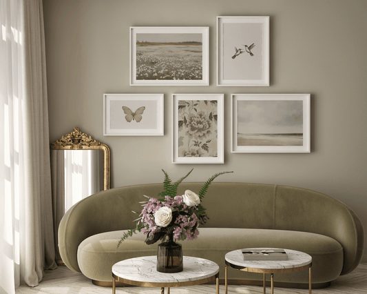 Neutral vintage nature gallery wall in a living room with framed landscape and botanical wall art above a curved sofa