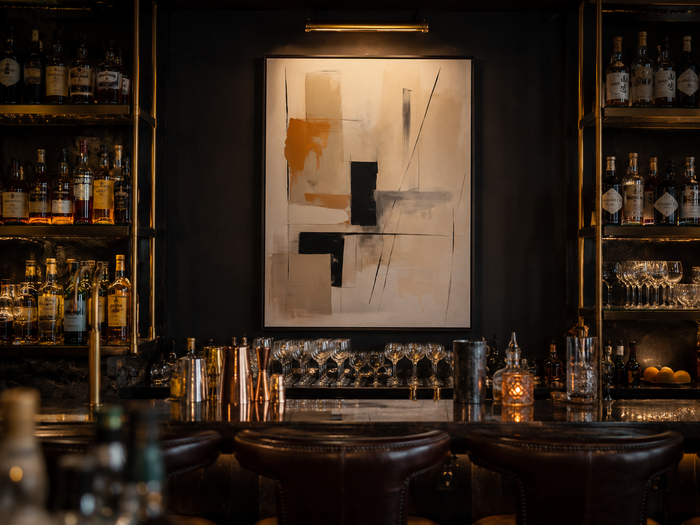 Wall art for bars: framed abstract print in cream, black, and orange behind a dark cocktail bar