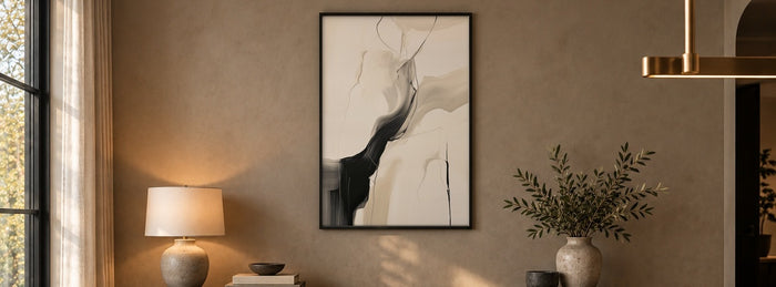 Black and beige abstract wall art in a thin black frame above a walnut sideboard with a table lamp and olive branches