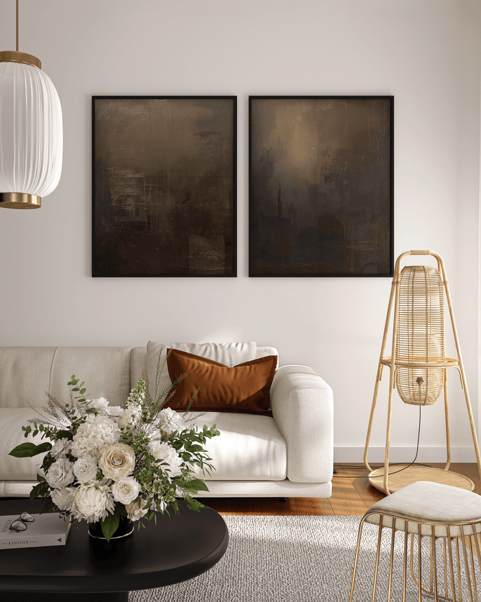 dark neutral abstract wall art in black, charcoal and brown tones styled above a cream sofa with a brown accent pillow, white floral arrangement and warm modern decor in a bright living room