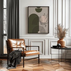 Abstract arch and botanical wall art in a black frame above a tan leather accent chair with pampas grass