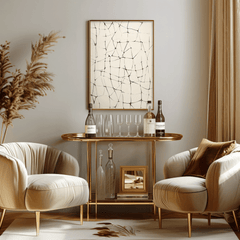 Abstract line grid wall art in black on beige with gold frame styled above a brass bar cart with glassware between two neutral lounge chairs