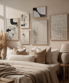 Minimalist gallery wall featuring abstract line grid wall art in black on beige above a neutral bed with layered beige pillows, linen duvet, and pampas grass