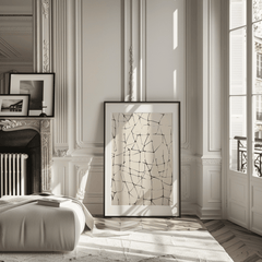 Large abstract line grid wall art in black on beige leaning on the floor in a classic Parisian-style room with fireplace, tall windows, and decorative molding