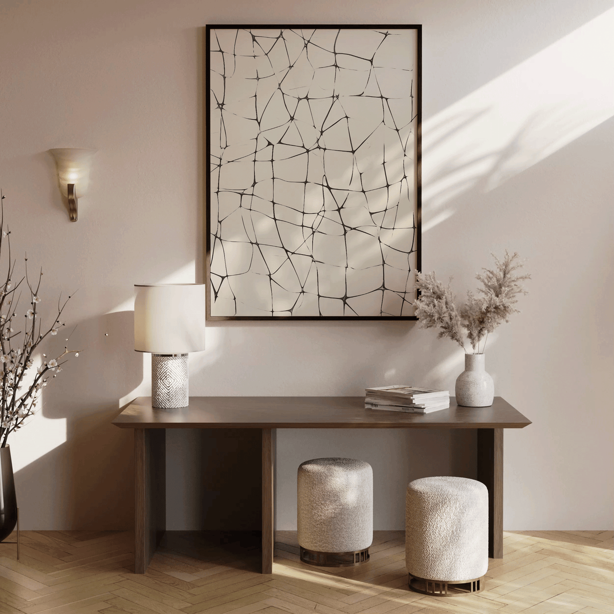 Abstract line grid wall art print in black on beige displayed above a modern wooden console table with ceramic lamp, stacked books, pampas in vase, and two textured ottomans