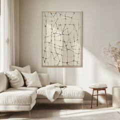 Oversized abstract line grid wall art in black on beige with a light oak frame hung above a cream sectional in a bright neutral living room with dried florals