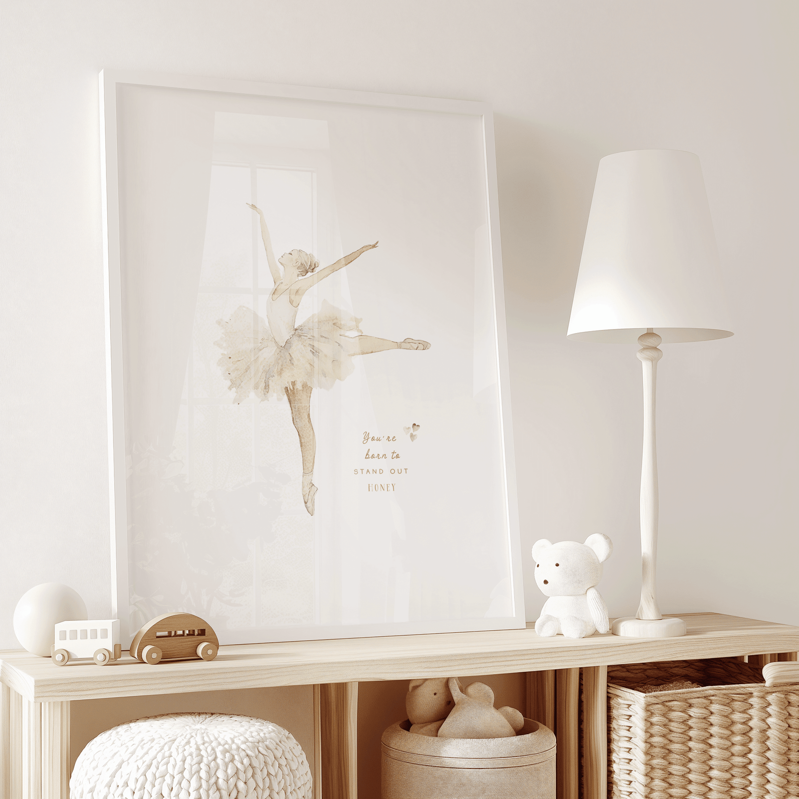 framed white vintage ballerina with beige and cream watercolor style and an inspirational quote that says, "you're born to stand out honey". little hearts are next to the quote in muted, neutral tones. Artwork is on a wooden shelf in a toddler or kid's play room; perfect for girl's nursery.