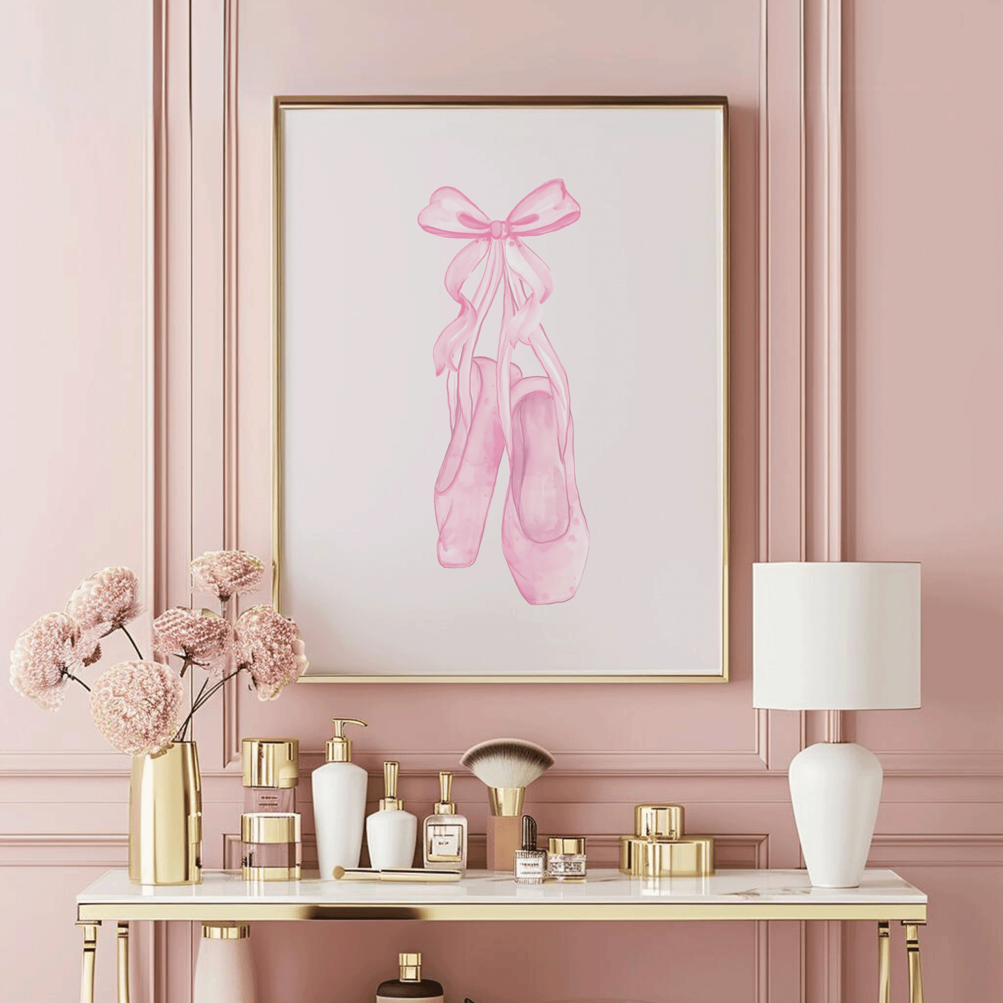 A framed art print featuring a watercolor illustration of pink ballet slippers, displayed on a pink wall above a styled vanity table.