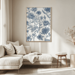 Blue and white floral print in a natural frame above a cream sofa in a sunlit neutral living room