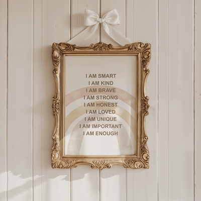 Boho rainbow affirmations print in an ornate gold frame hung with a white ribbon bow on a cream panelled wall