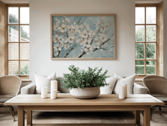 Large cherry blossom wall art with white blossoms on blue background framed in light wood, styled in a bright sunroom or living room