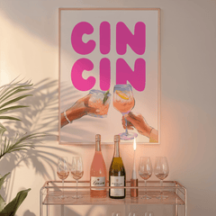Cin cin wall art in a natural frame above a glass bar cart with wine bottles and a candle
