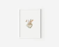 Close-up of a white framed bunny nursery wall art print featuring a white rabbit in a vintage floral teacup surrounded by butterflies and blush flowers