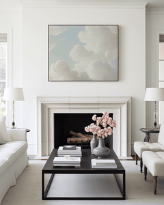 Large vintage white and blue cloud canvas wall art with a black frame above fireplace in neutral modern living room