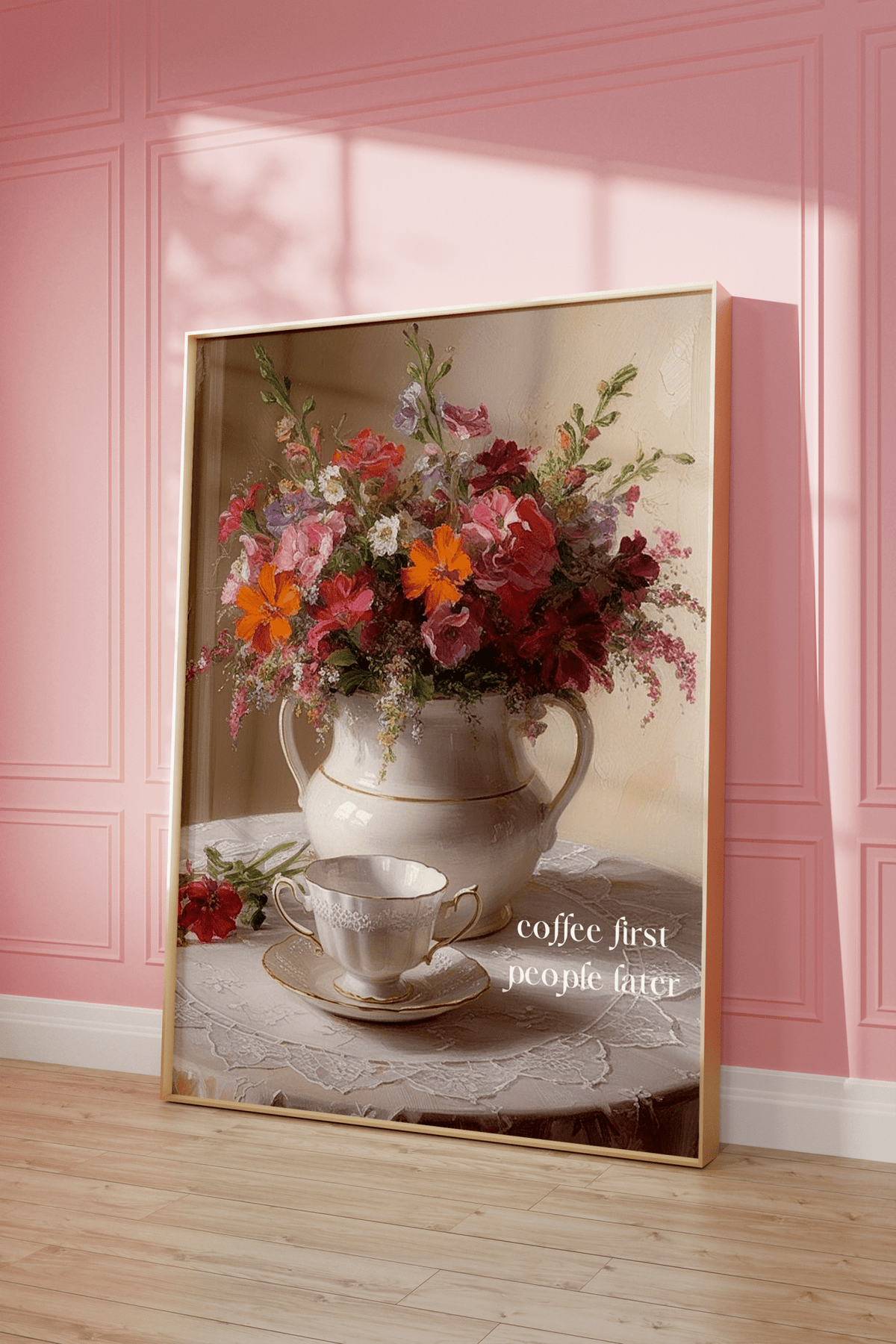 Framed wall art with flowers in a vintage vase and a teacup on a table against a pink wall.