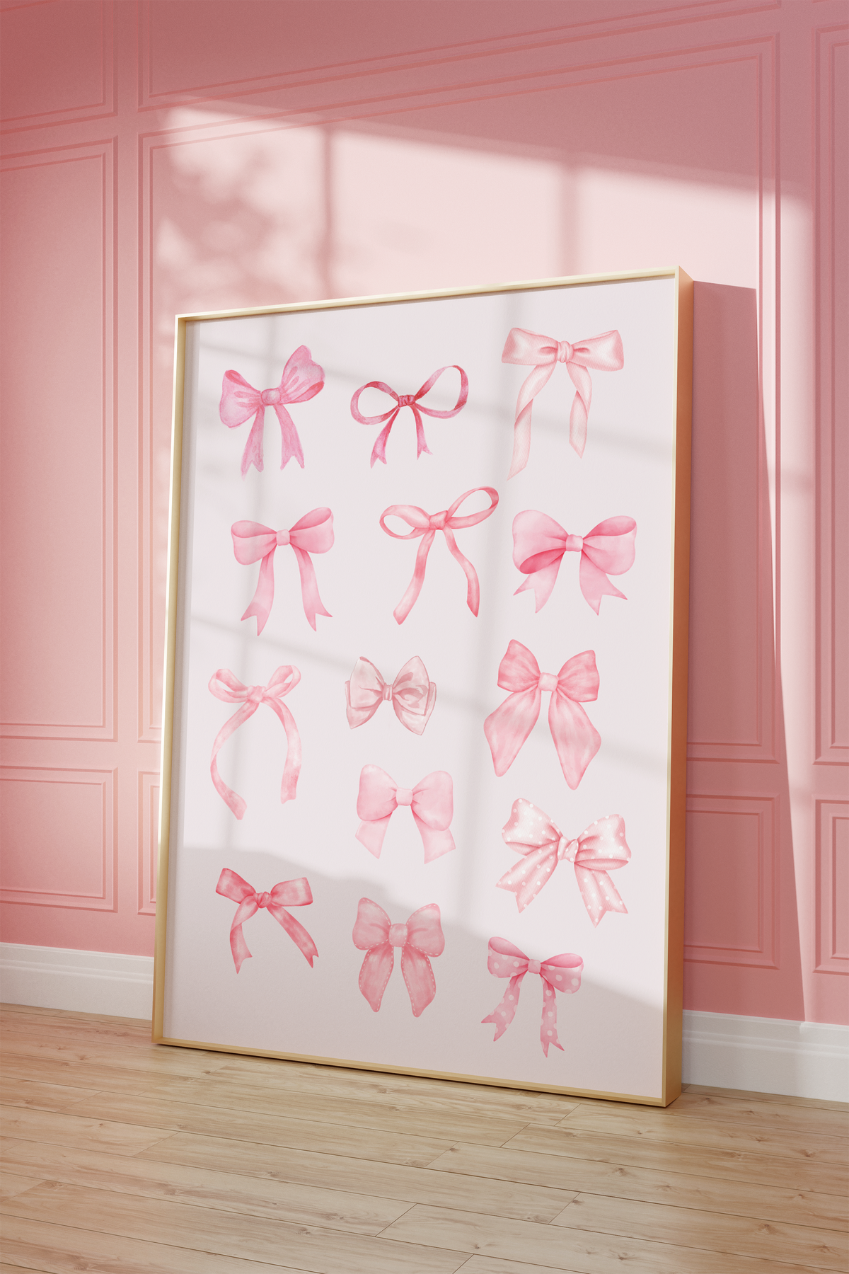 A large framed art print featuring watercolor pink ribbon bows on a white background, leaning against a pink paneled wall on a light wood floor.
