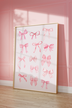 A large framed art print featuring watercolor pink ribbon bows on a white background, leaning against a pink paneled wall on a light wood floor.
