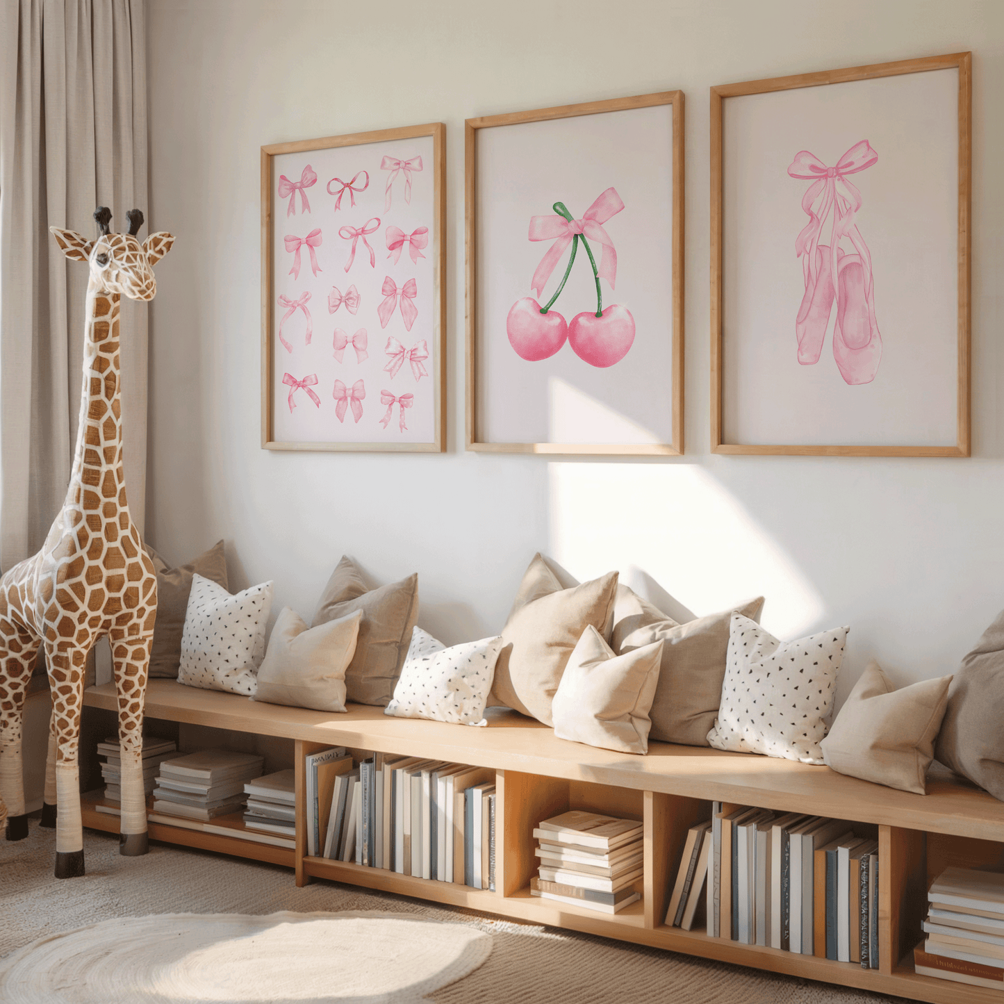 A styled children's room corner with three framed wall prints above a wooden bench. The prints show pink ballet bows, cherries with pink bows, and pink ballet slippers.