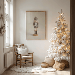 Framed nutcracker Christmas artwork hanging beside a flocked Christmas tree in a cozy corner with a wood chair and layered neutral textiles