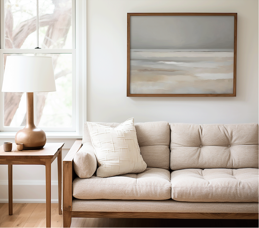 Beige sofa in a living room with a side table and framed abstract painting of a coastal beach in beige and soft blue tones.
