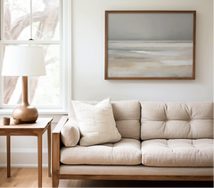 Neutral coastal beach print in beige and soft blue above a beige sofa in a living room with a side table