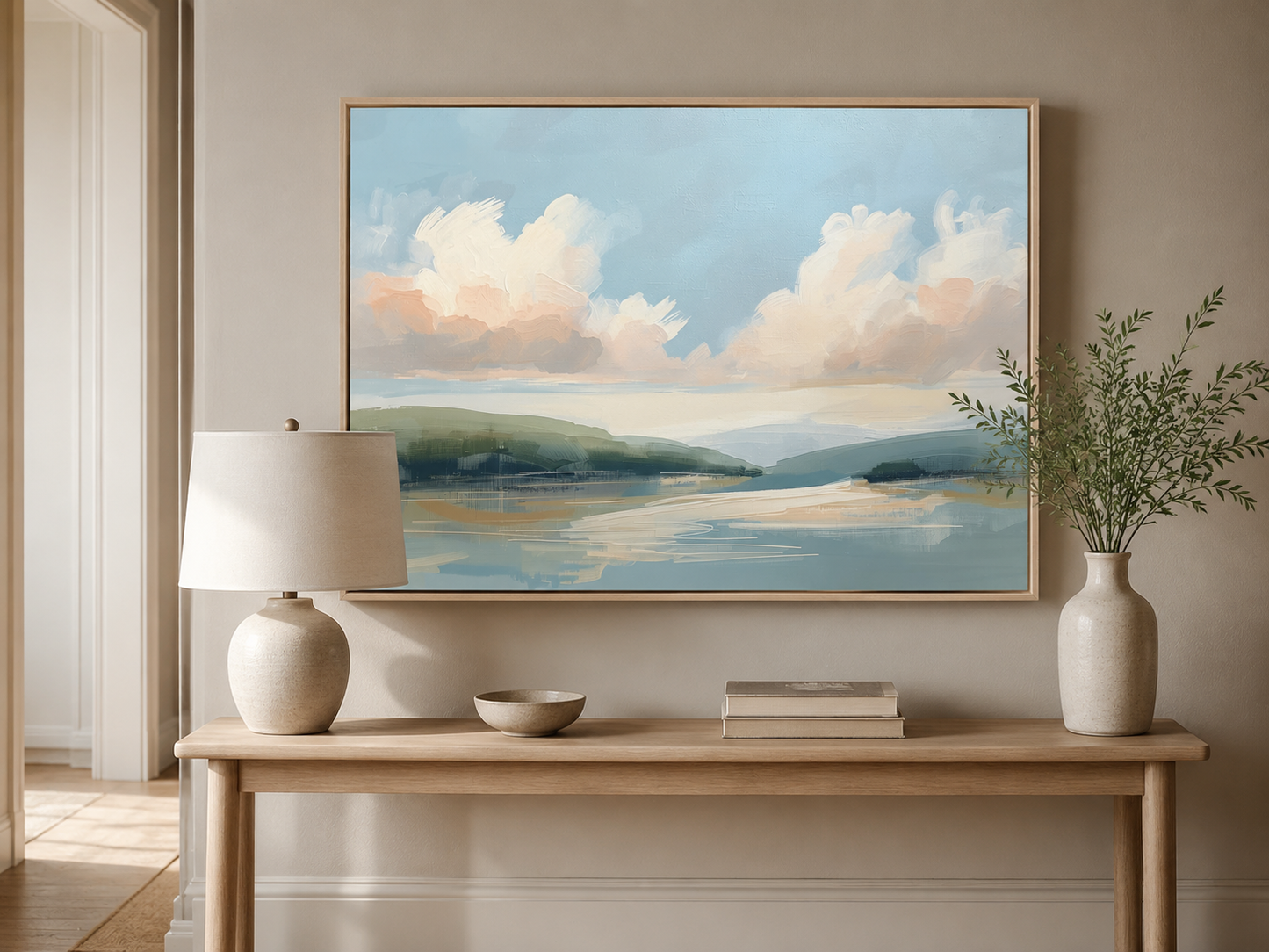 Large framed pastel landscape wall art above a light wood console table in a warm neutral entryway with ceramic decor and greenery.