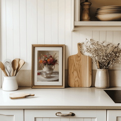 Floral coffee wall art in a natural wood frame leaning on a white kitchen counter beside a cutting board