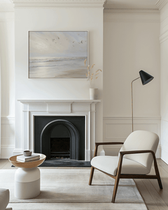 Framed beach ocean print with gentle waves and flying seagulls displayed above white fireplace — elegant neutral wall art for living room decor