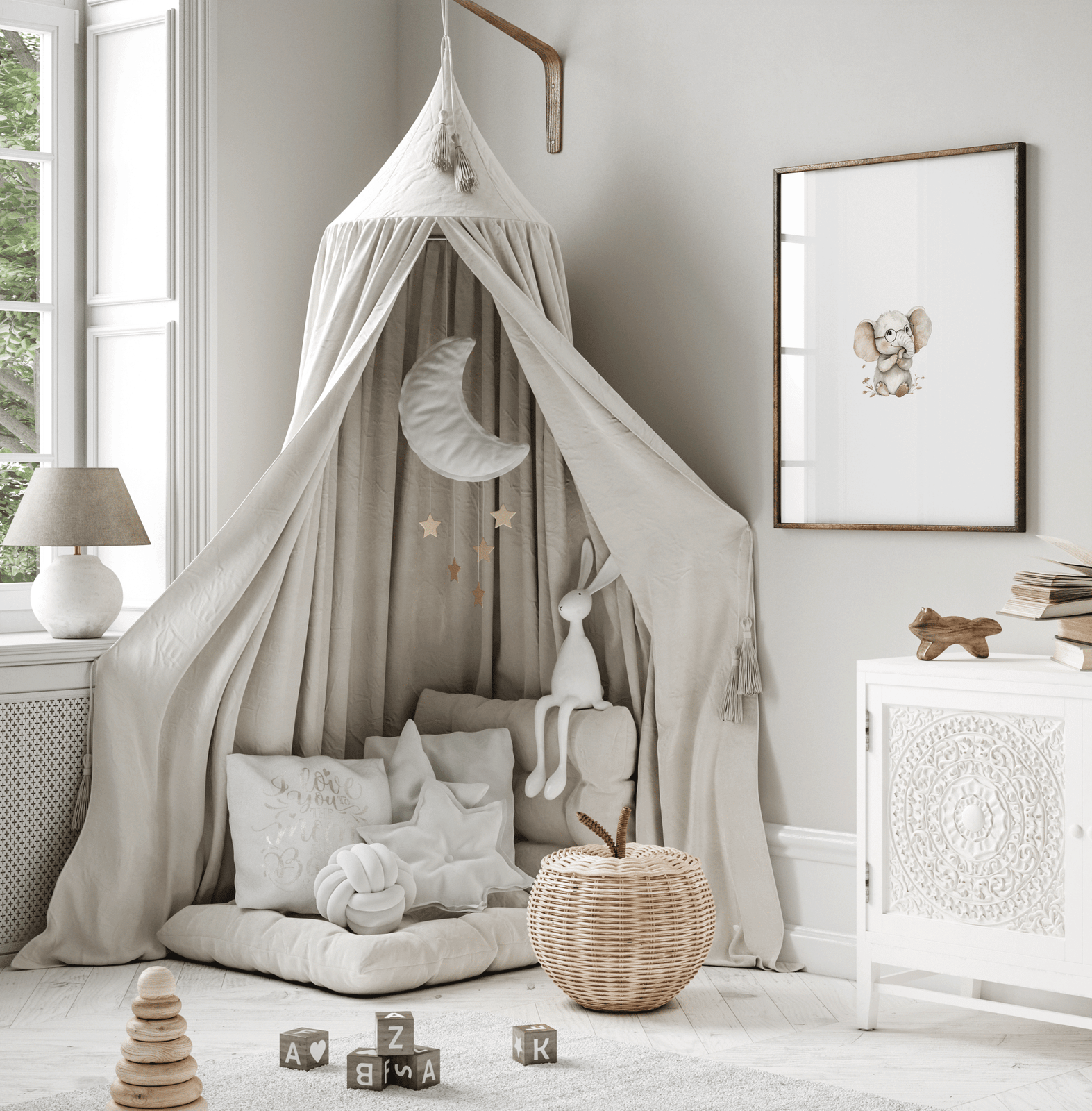 Framed elephant wall art hanging beside gray canopy and cozy little boy or girl nursery or play room reading nook with plush decor.