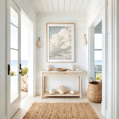Nautical-themed entryway interior with shell decor, framed blue sky clouds wall art print above console table