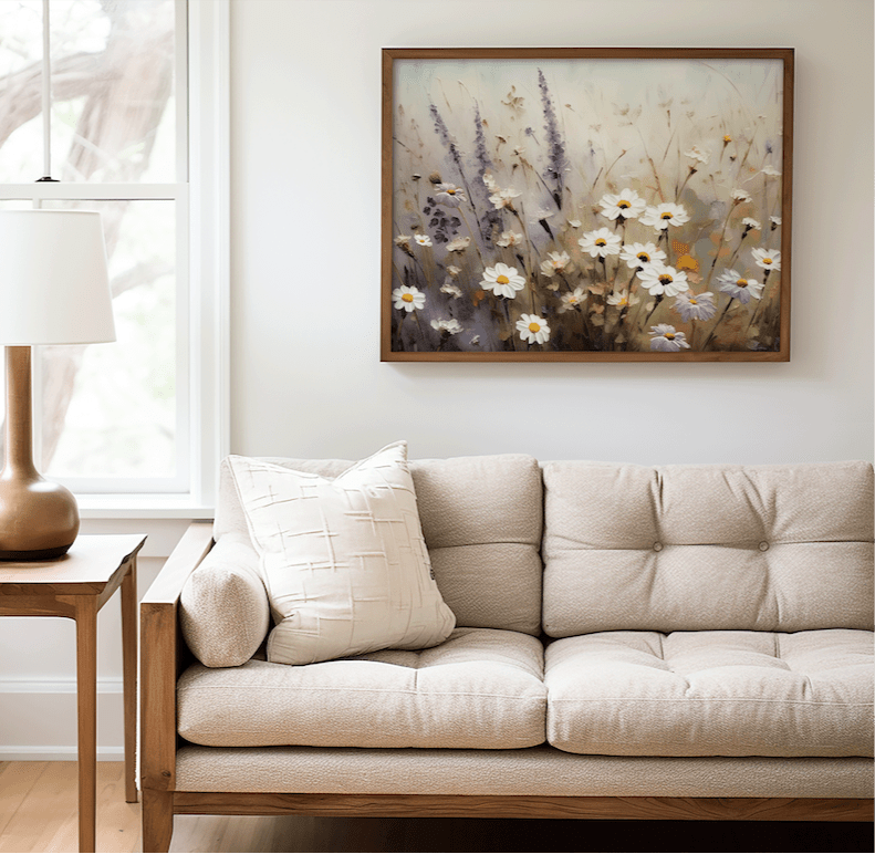 Framed wildflower meadow art with white daisies and light purple lavender hanging above a beige sofa in a cozy living room. 