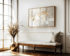 Gallery-wrapped canvas print of gold and beige abstract artwork with smooth metallic finish. Framed wall art above a wooden tufted bench in a hallway next to a large window and floor vase with dried flowers.