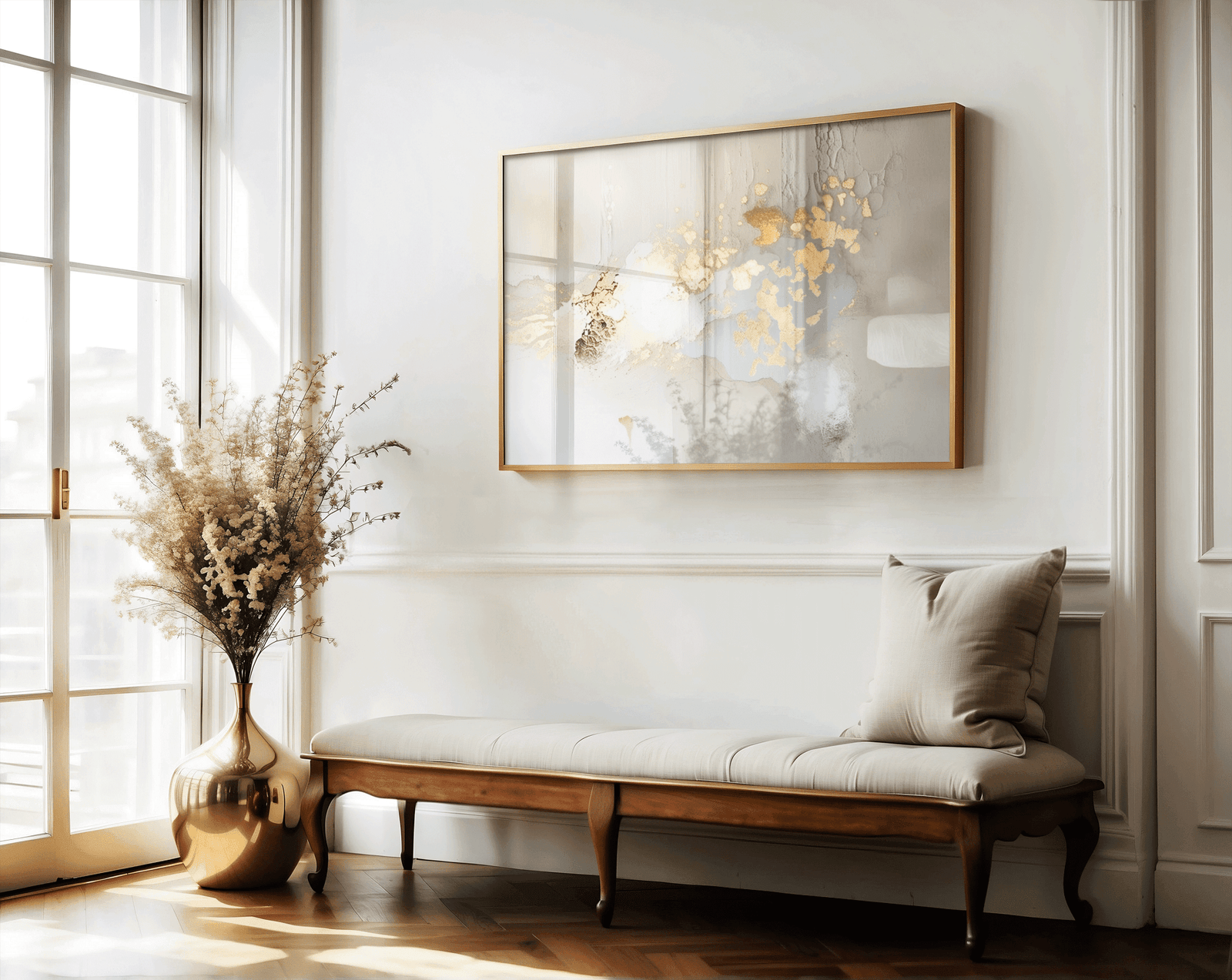 Gallery-wrapped canvas print of gold and beige abstract artwork with smooth metallic finish. Framed wall art above a wooden tufted bench in a hallway next to a large window and floor vase with dried flowers.
