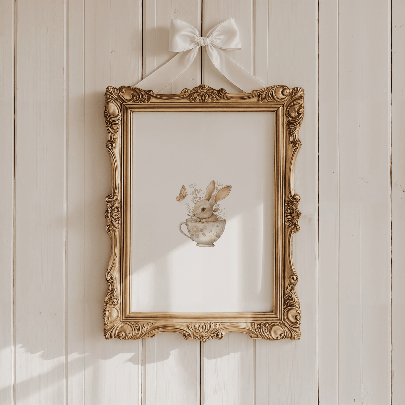 Gold framed bunny nursery wall art print featuring a watercolor rabbit in a floral teacup with butterflies, accented with a white ribbon bow