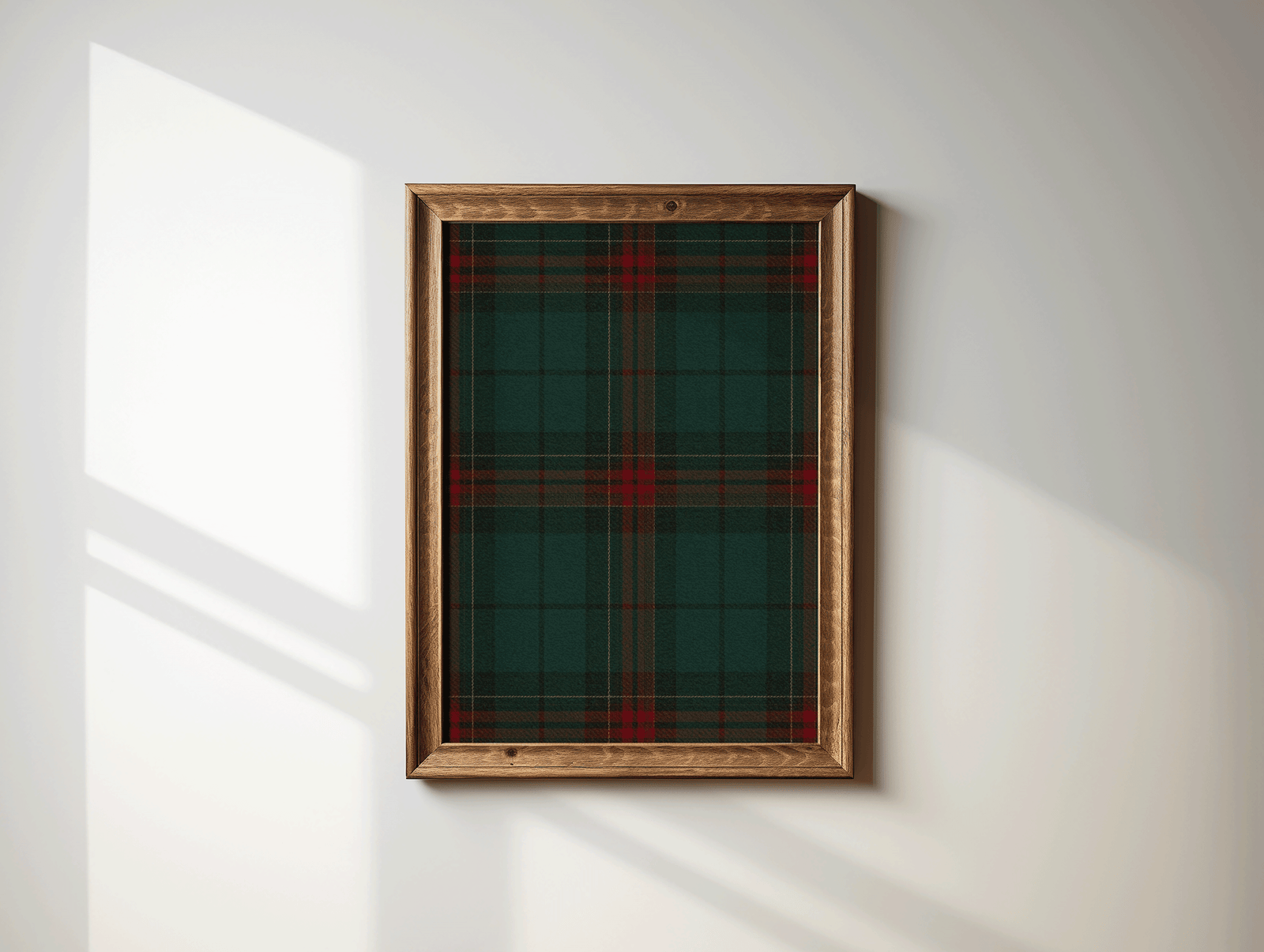 Green and red plaid wall art in a brown wood frame on a sunlit white wall