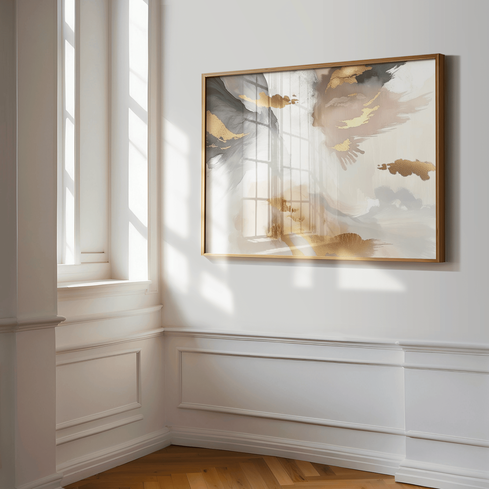 Large abstract wall art print framed on a white wall with wainscotting and nature sunlight filtering through a window. The artwork has a mix of light pink, gold accents, white, beige/cream and grey tones with a wooden frame.