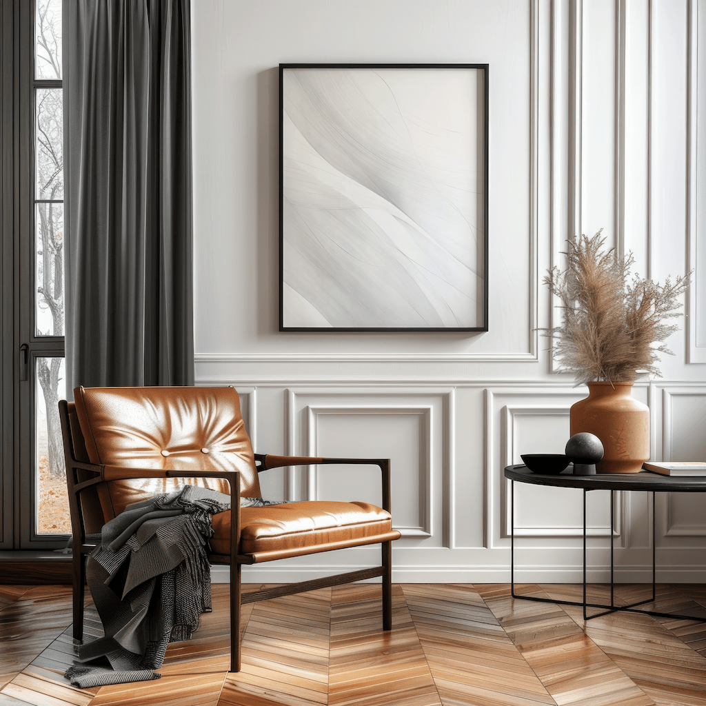 Large neutral abstract wall art in white and grey tones framed in black above a tan leather armchair in a contemporary living room
