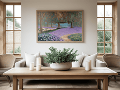 Purple lavender meadow nature landscape wall art framed with painterly countryside path and serene tones. Impressionist style with an abstract design and a light wooden frame hanging above a white couch in a minimal living room with wooden accents.