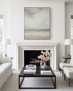 Modern living room with a fireplace, coffee table, and vintage muted beach coastal landscape framed above fireplace.