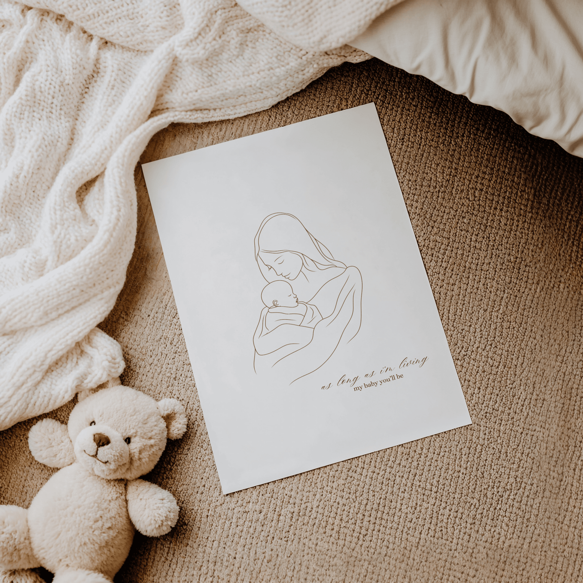 Mom and baby line drawing print lying on a knit blanket beside a teddy bear