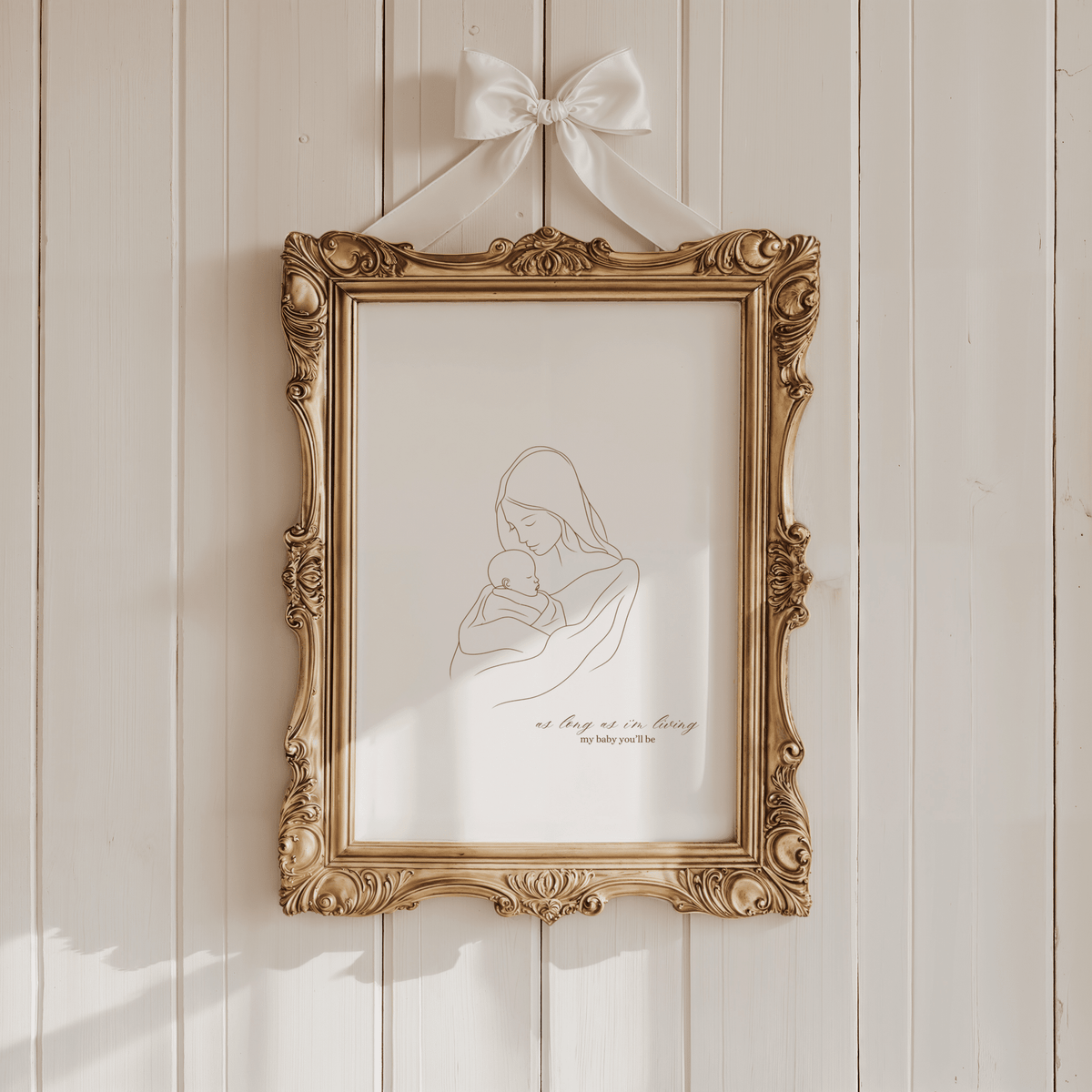 Mother and baby line art print in an ornate gold frame hung with a white ribbon bow on a cream panelled wall