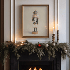 Framed vintage blue and gold nutcracker print above a holiday mantel with evergreen garland, candles and warm lights