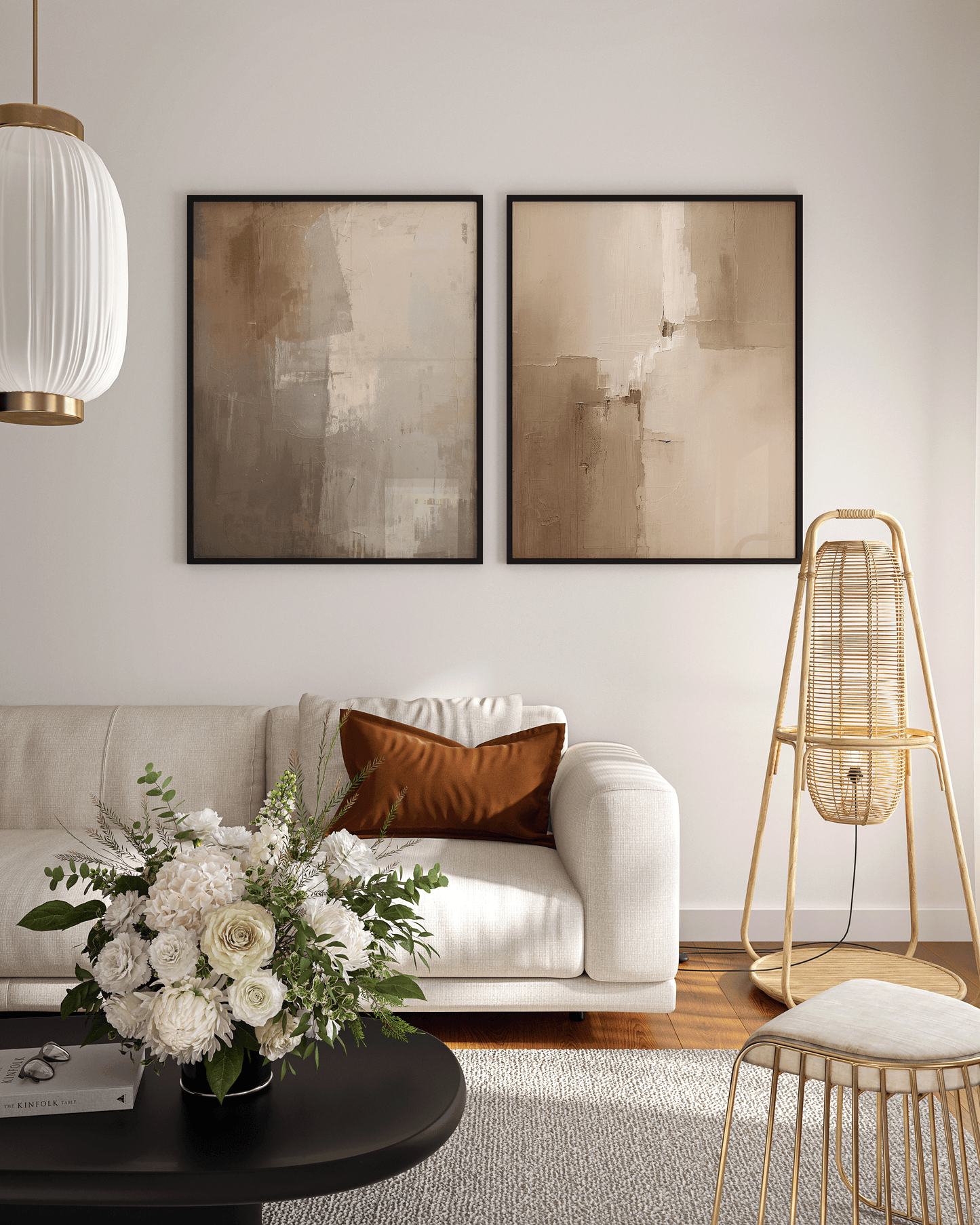 pair of moody beige and brown abstract wall art prints in black frames displayed above a light sofa in a bright living room with floral arrangement and modern décor