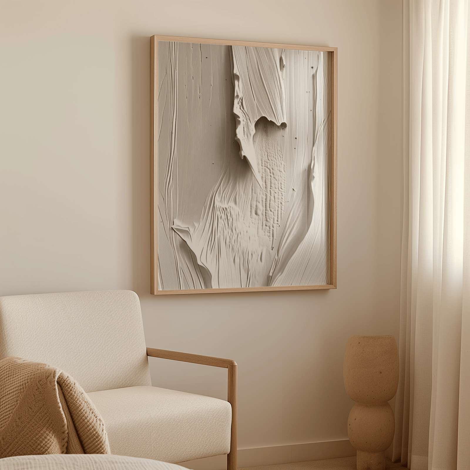 A natural wood-framed abstract wall art print with a mix of cream and beige, and faux-textured design, next to a light-colored chair in a neutral living room