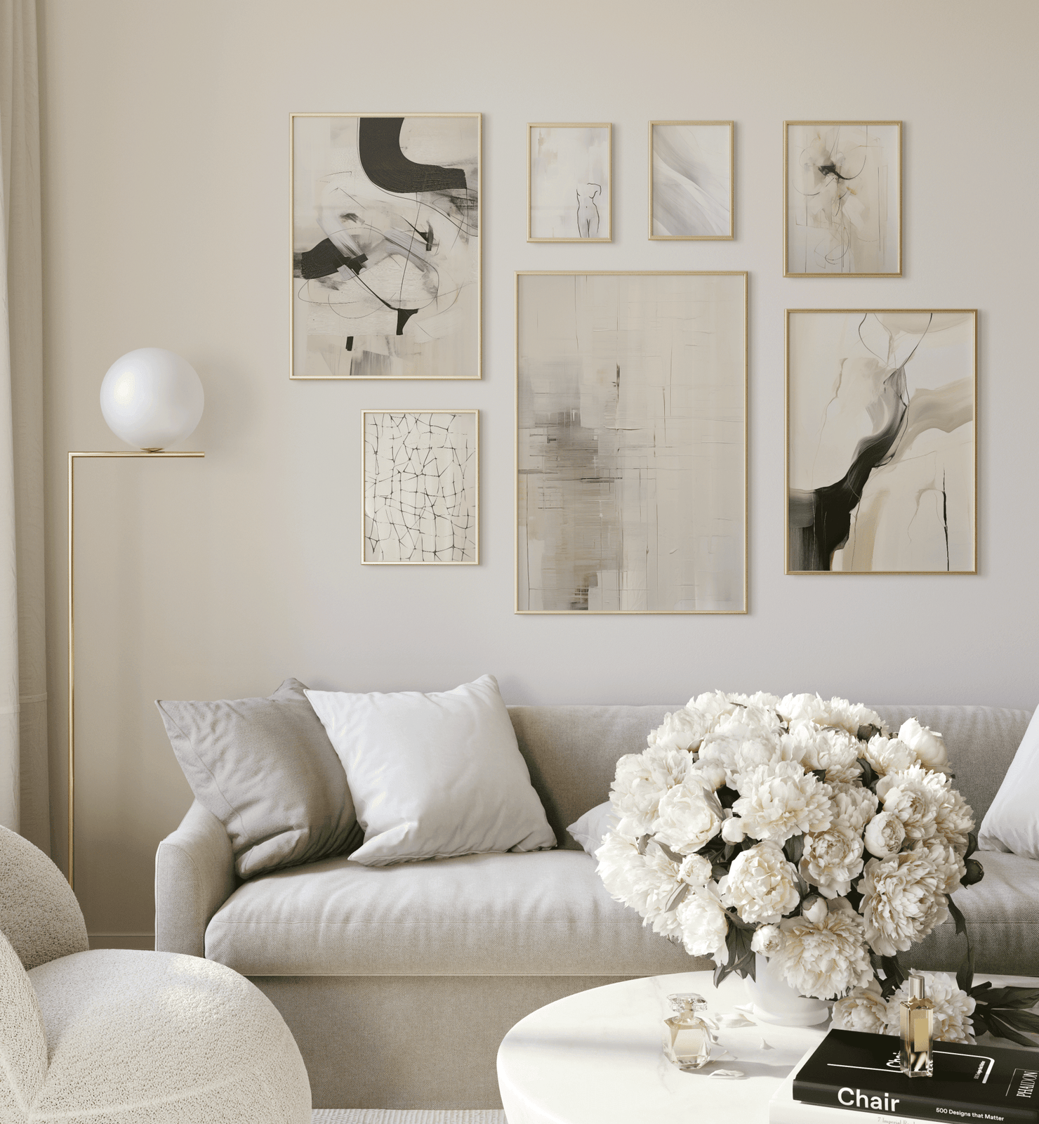 Neutral gallery wall above a light sofa with seven black-and-beige abstract prints in thin gold frames; white peony bouquet on round coffee table.
