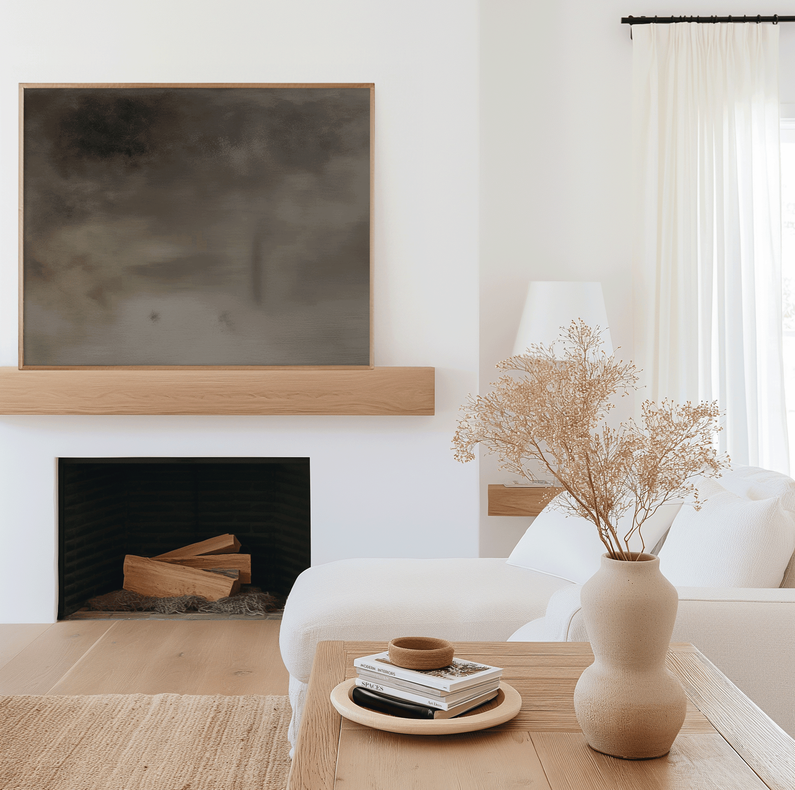 Neutral moody abstract wall art in a natural wood frame hanging above a modern fireplace in a bright minimalist living room with white furniture, wood accents, and dried floral decor.