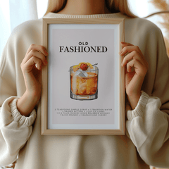 Woman in a cream sweater holding a framed Old Fashioned cocktail print